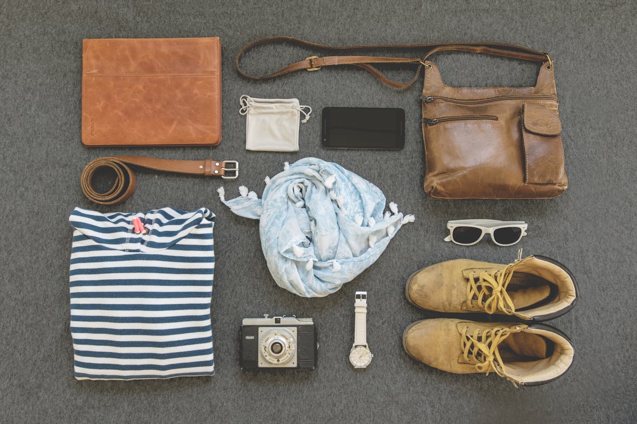 why-choose-us Vintage travel essentials flat lay with leather bags, shoes, camera, and clothing.